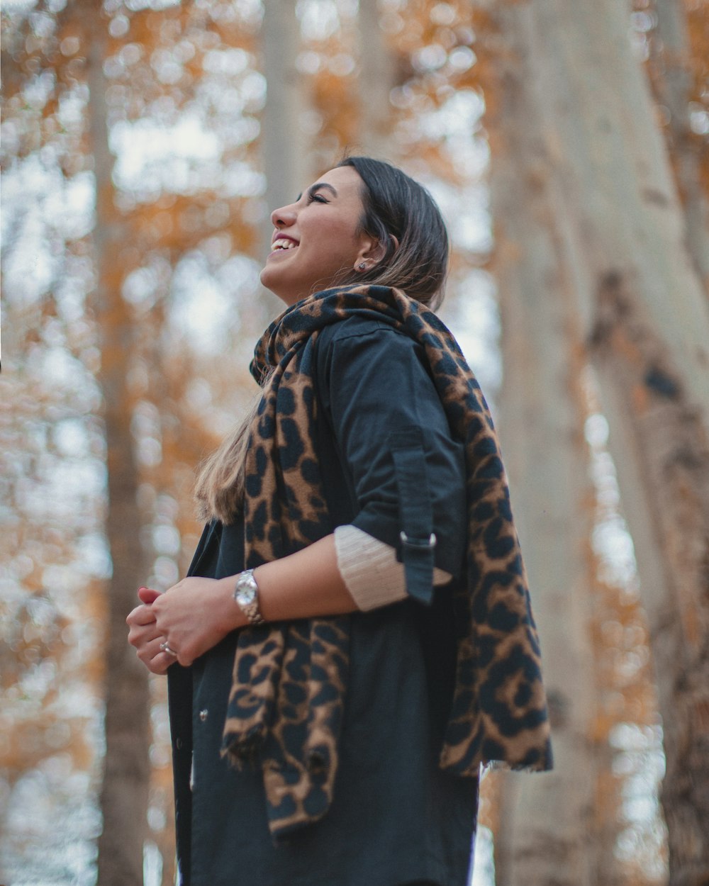 a woman standing in a forest with a scarf around her neck