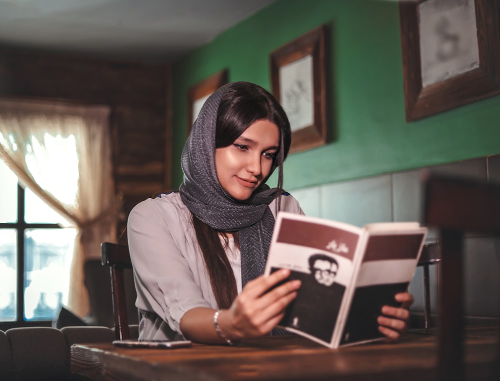 a woman sitting at a table reading a book