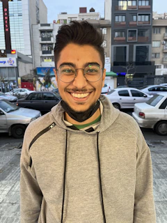 A smiling person wearing sleek eyeglasses, standing in a bright urban setting.