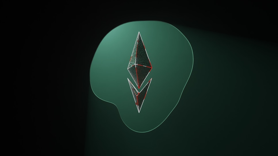 A stylized, geometric shape resembling the Ethereum logo is set against a dark green background. The shape is made of metallic, reflective surfaces with thin red outlines. It sits atop a larger, soft-edged shape in a lighter shade of green.