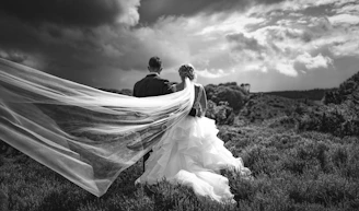 a bride and groom walking through a field under a cloudy sky