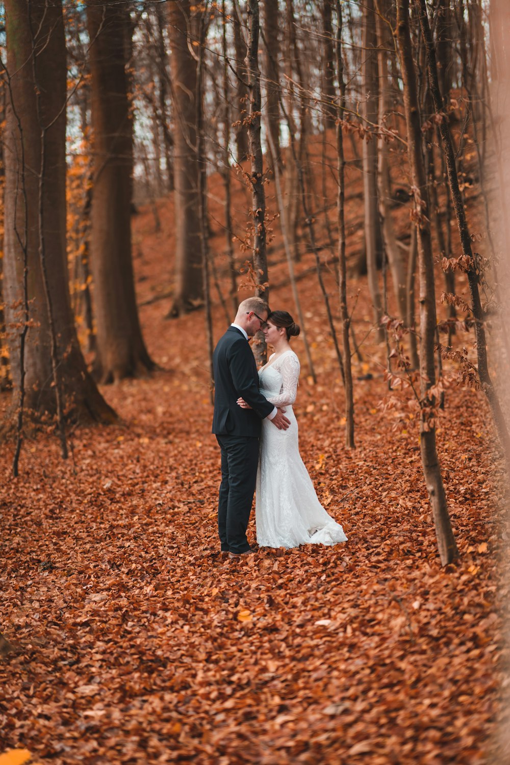 a bride and groom standing in the woods