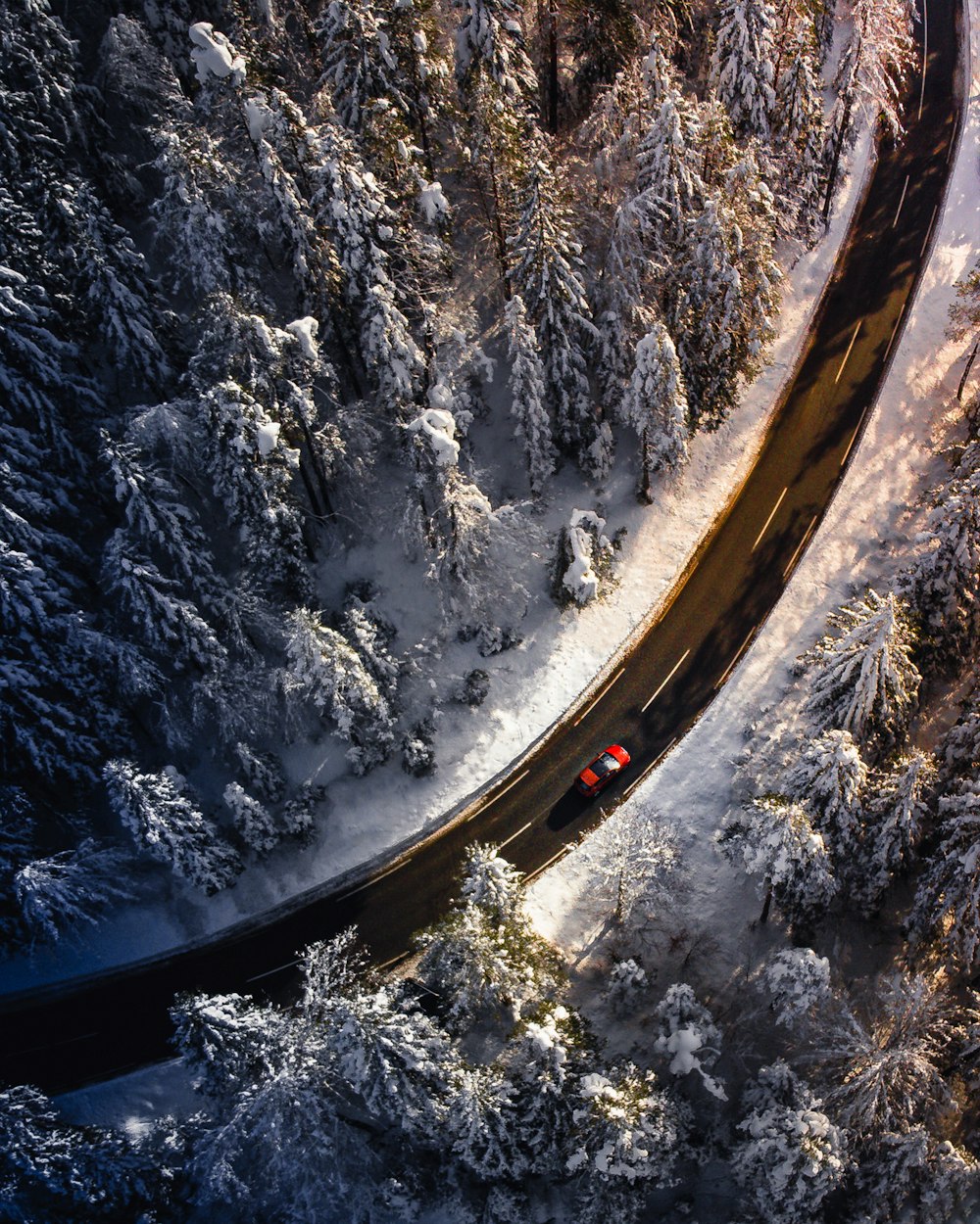 an aerial view of a road in the middle of a snowy forest