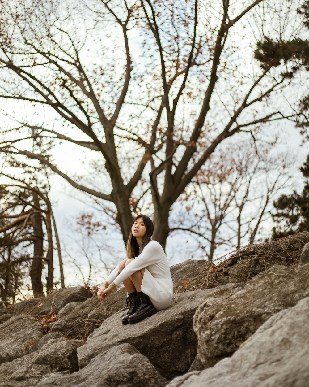 a woman sitting on top of a rock next to a tree