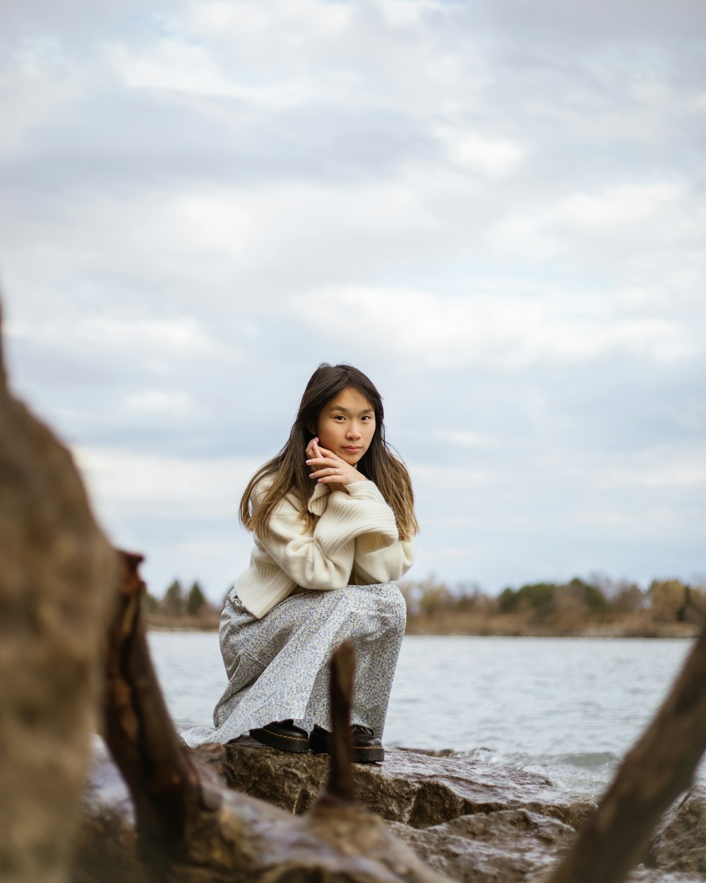 a woman is sitting on a rock by the water