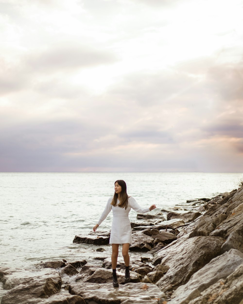 a woman in a white dress standing on rocks near the ocean