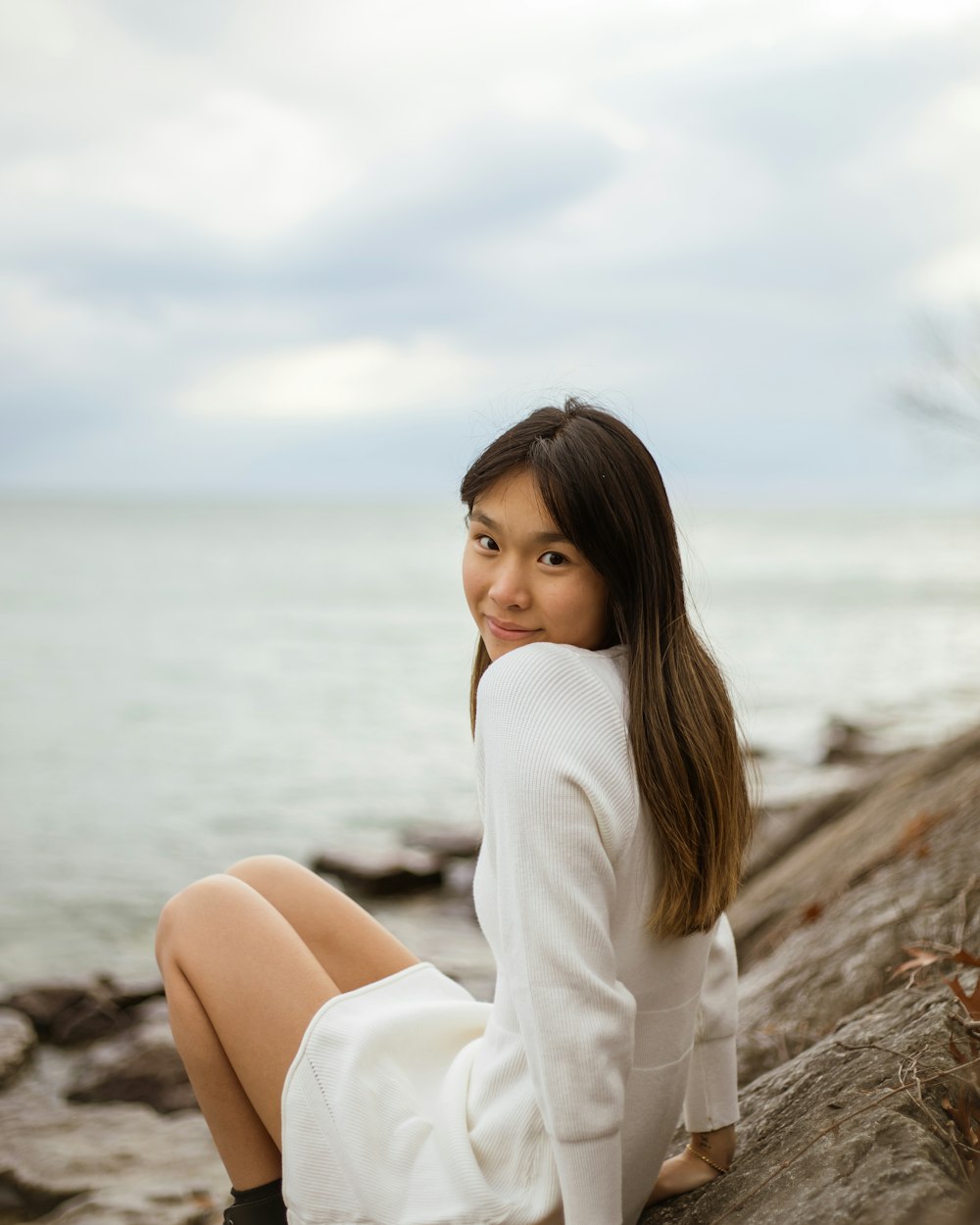 a woman is sitting on a rock by the water