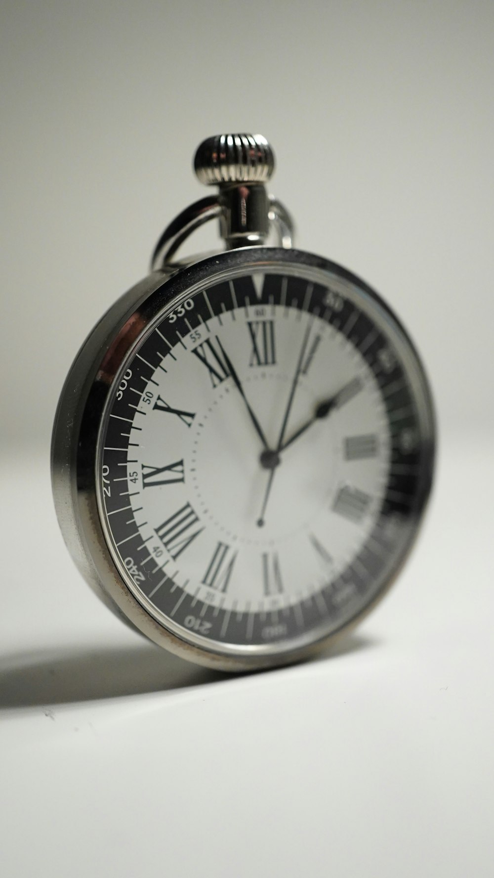 a silver pocket watch with roman numerals on a white surface