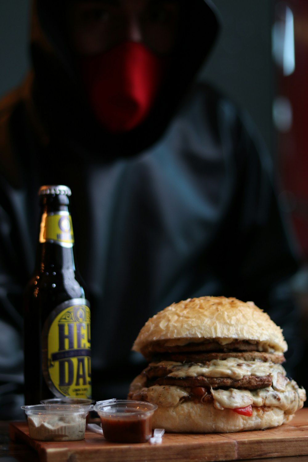 a man in a hoodie sitting at a table with a sandwich and a beer