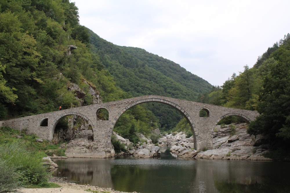 a stone bridge over a river surrounded by mountains