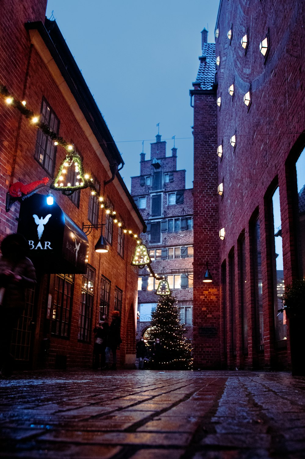 Un callejón de ladrillos con luces navideñas y un árbol de Navidad