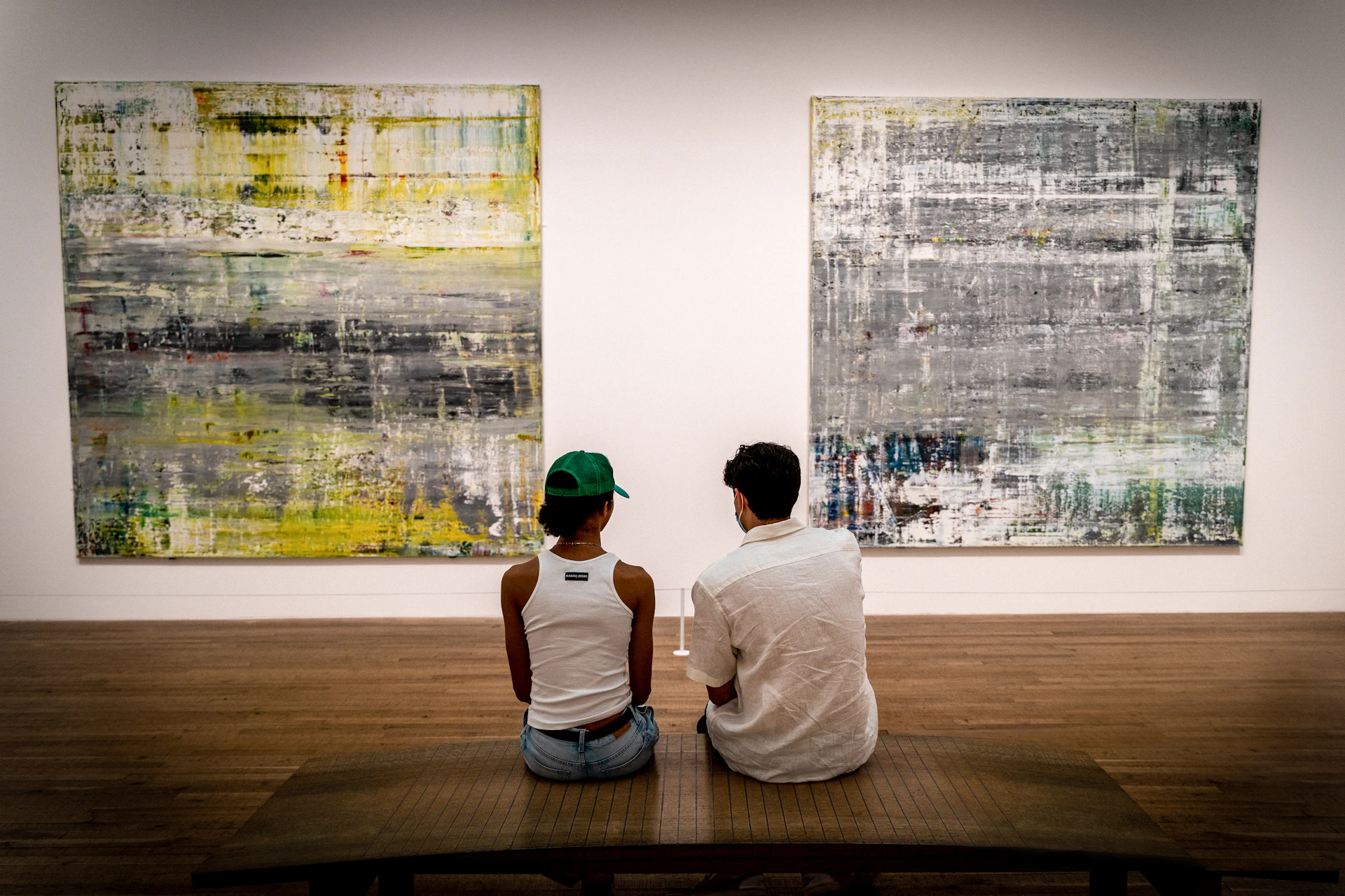a man and a woman sitting on a bench in front of paintings