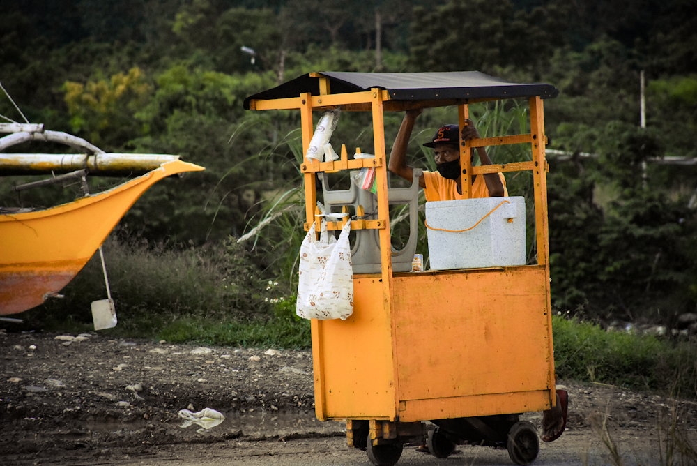 a man driving a yellow truck with a boat in the background