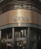 A modern bookstore with a curved, sleek architectural design featuring large glass windows and metal panels. The signage displays both Japanese characters and English text that reads 'TSUTAYA BOOKS'.