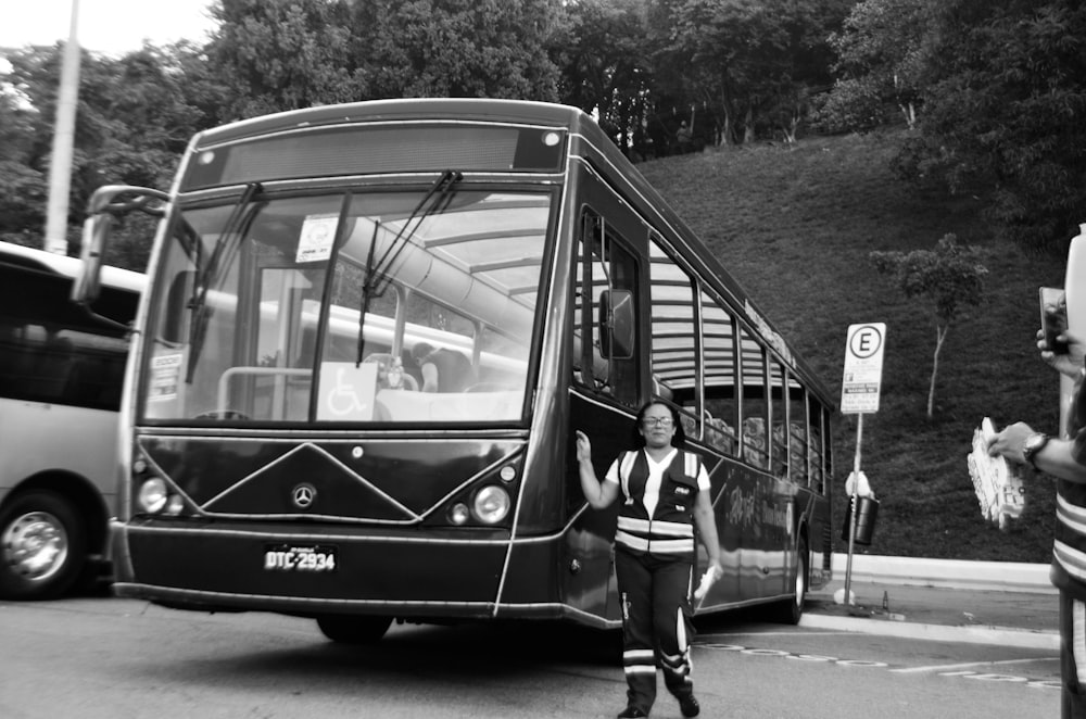 a black and white photo of a man standing in front of a bus