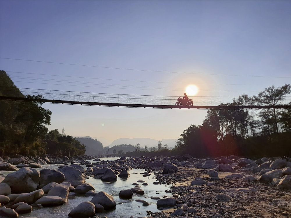 a man riding a motorcycle across a bridge over a river