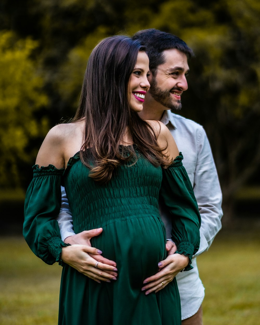 a pregnant woman in a green dress standing next to a man