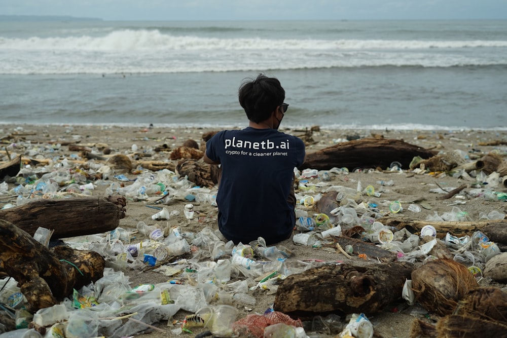 a young boy sitting on a beach covered in trash