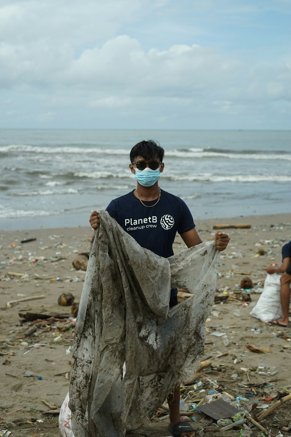 a man wearing a face mask holding a plastic bag on a beach