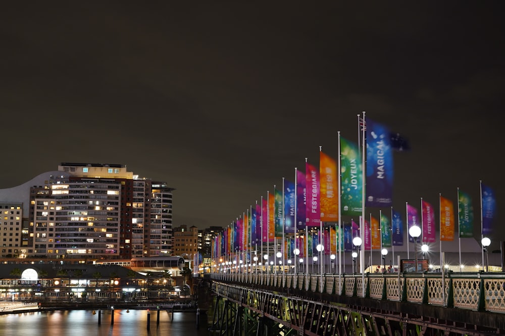 a night scene of a city with a bridge and colorful flags