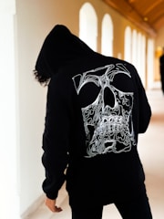 a person wearing a black hoodie with a white skull on it