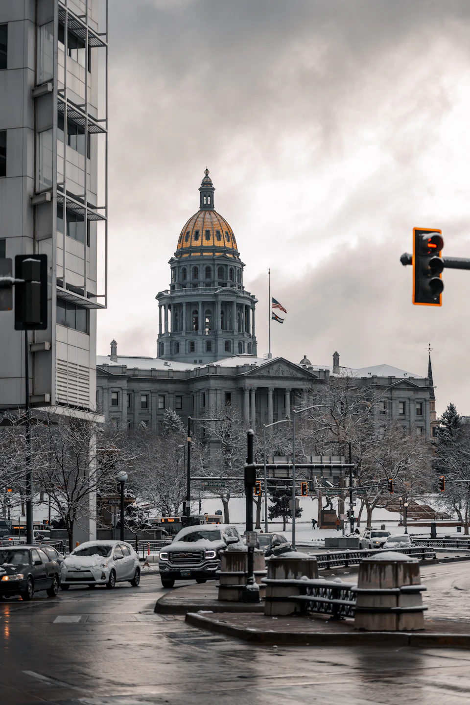 The image depicts a city street scene with a large, ornate building featuring a golden dome and columns at its center. The building is part of the historic Fort Worth, Texas City Square complex, which includes other buildings surrounding it. The sky above is overcast, casting a soft light on the scene below. Cars are parked along the street, and traffic lights can be seen in the background.