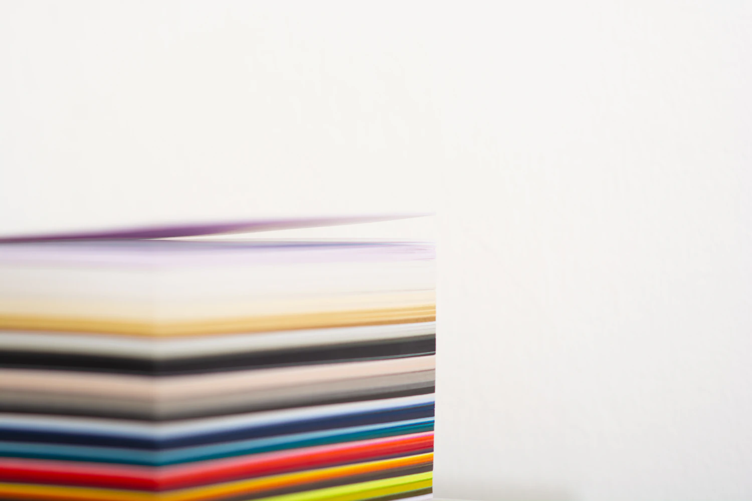 The cut edge of a block of coloured papers stacked in strict bands against a white ground