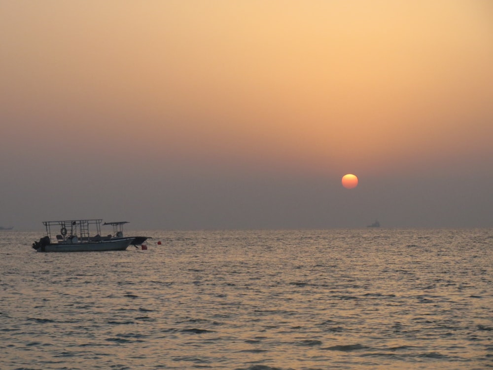 a boat in the ocean with the sun setting in the background