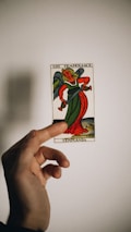 A hand holds a tarot card depicting an angelic figure with green and red robes. The card bears the title 'Temperance' with the number XIV at the top. The background is plain with a soft shadow cast by the hand and card.