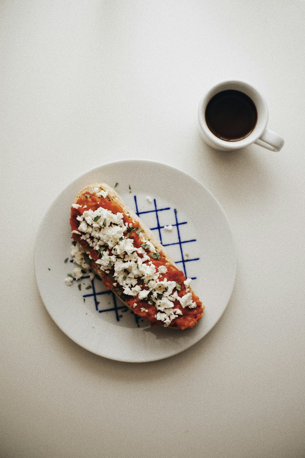 a white plate topped with a piece of pizza next to a cup of coffee