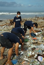 Volunteers picking up trash on a sunny beach with smiles and gloves.