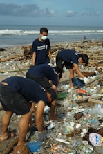 Volunteers cleaning a beach covered with plastic waste under a bright sky.