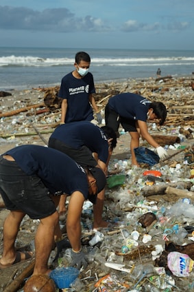 Volunteers cleaning a beach covered with plastic waste under a bright sky.