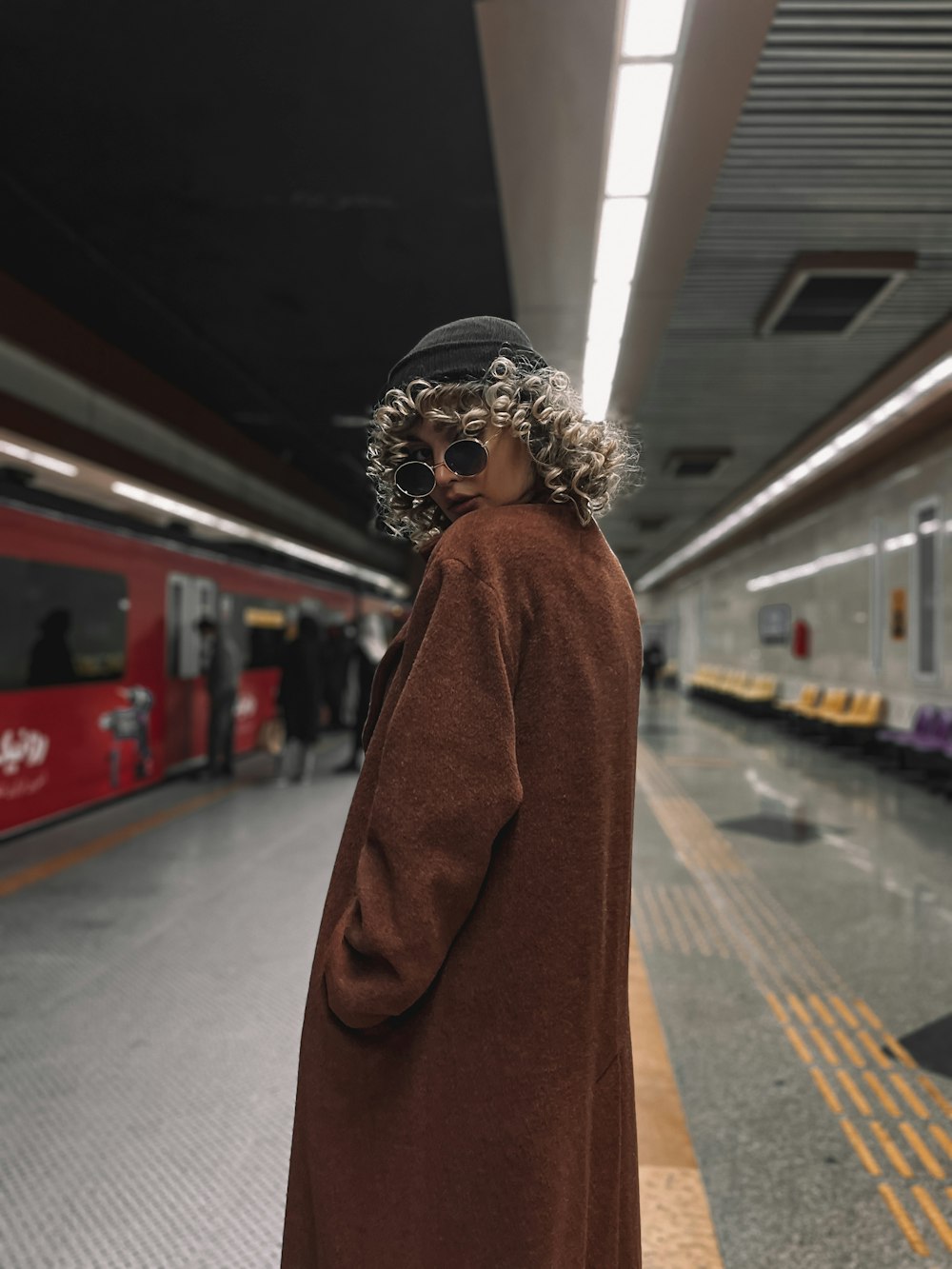 a man with curly hair and a hat standing in a train station