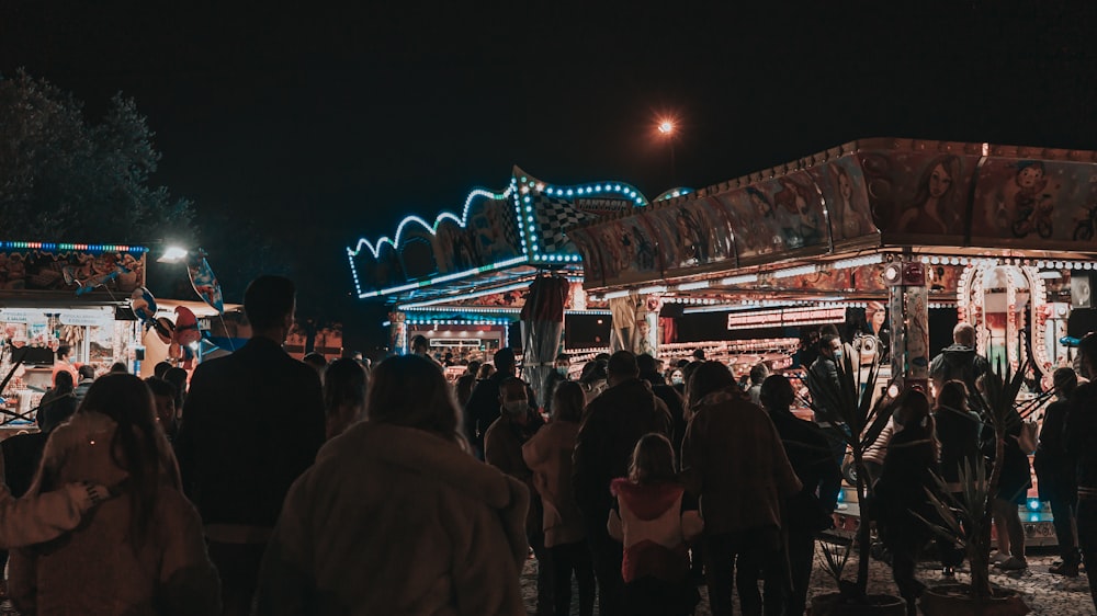 a crowd of people standing around a fairground at night