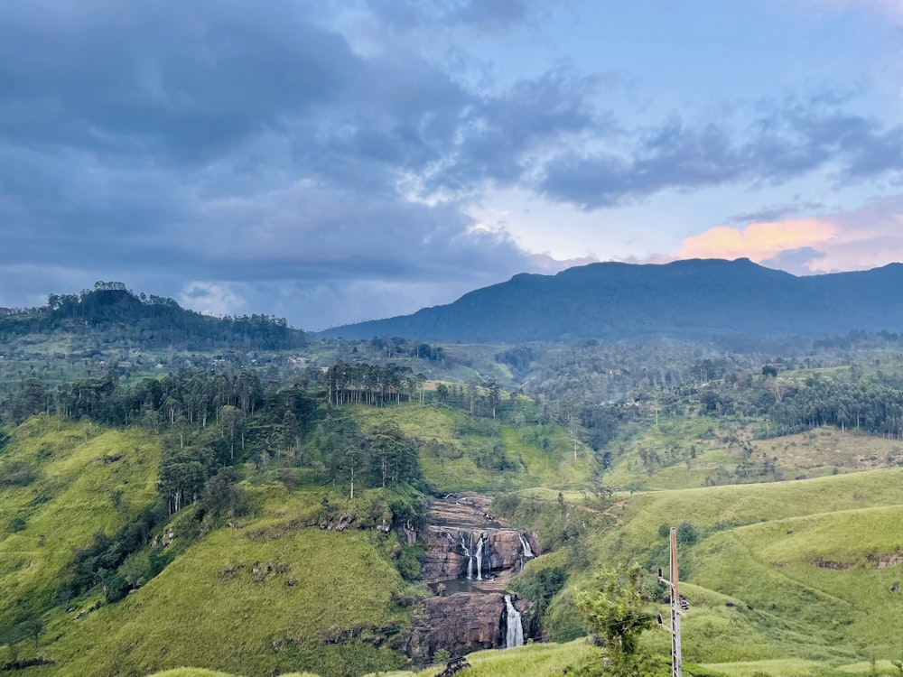 a lush green hillside with a waterfall in the distance