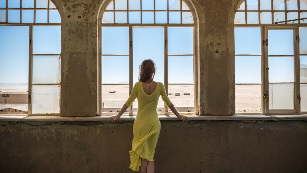 a woman in a yellow dress looking out a window