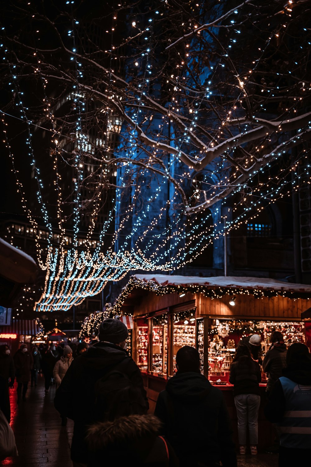a crowd of people walking down a street covered in christmas lights