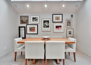 a dining room table with white chairs and pictures on the wall