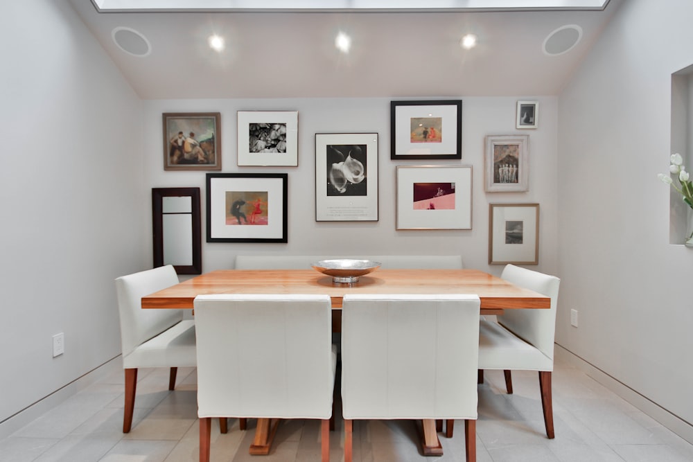 a dining room table with white chairs and pictures on the wall