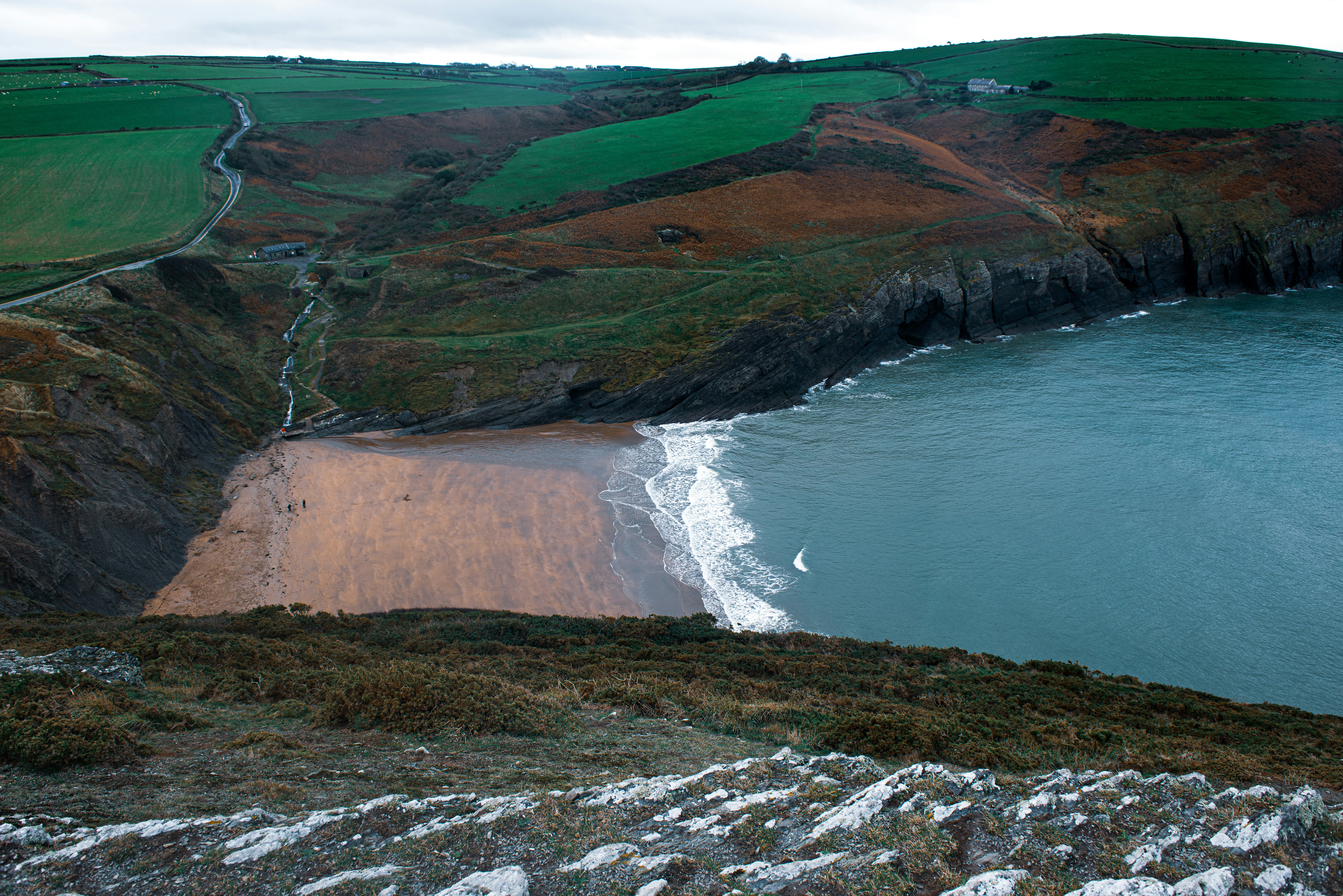 a sandy beach next to a green hillside