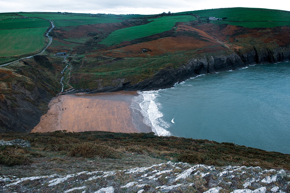 a sandy beach next to a green hillside