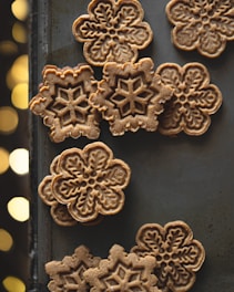 A collection of intricately patterned cookies set against a dark background. The cookies feature detailed snowflake designs, creating a festive and artistic appearance.