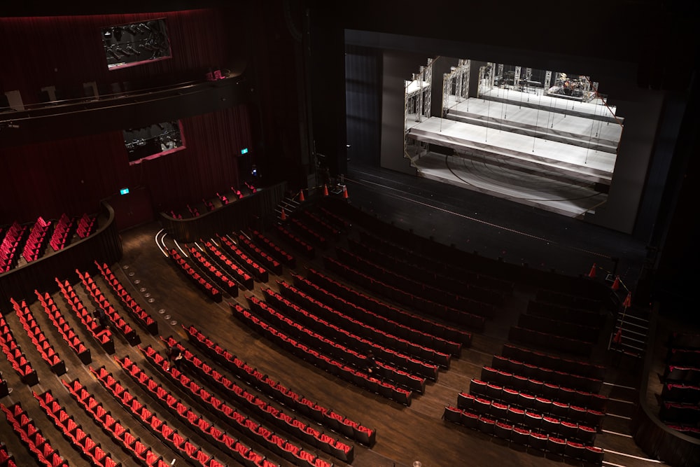 an empty auditorium with red seats and a projector screen