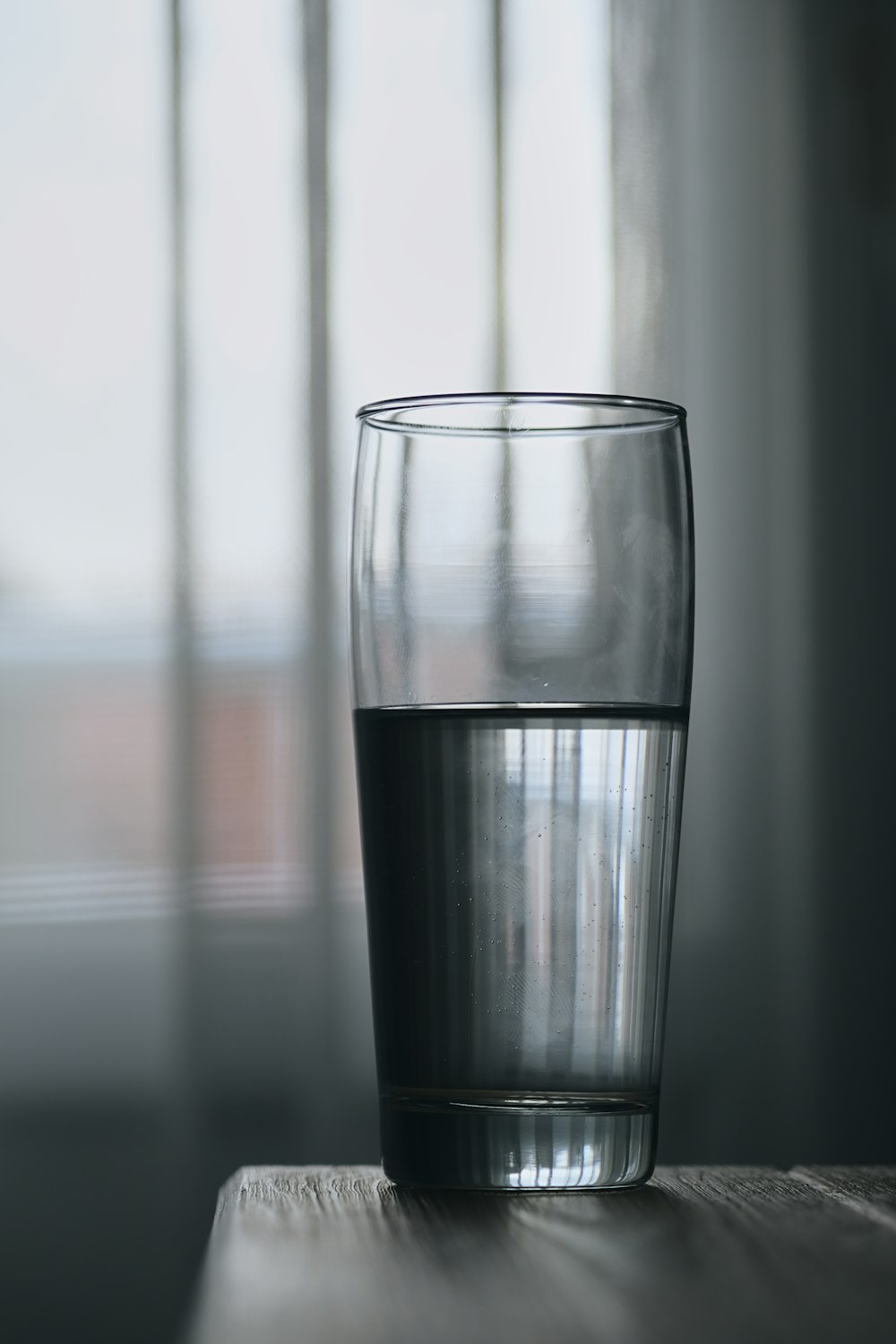 a glass of water on a table in front of a window