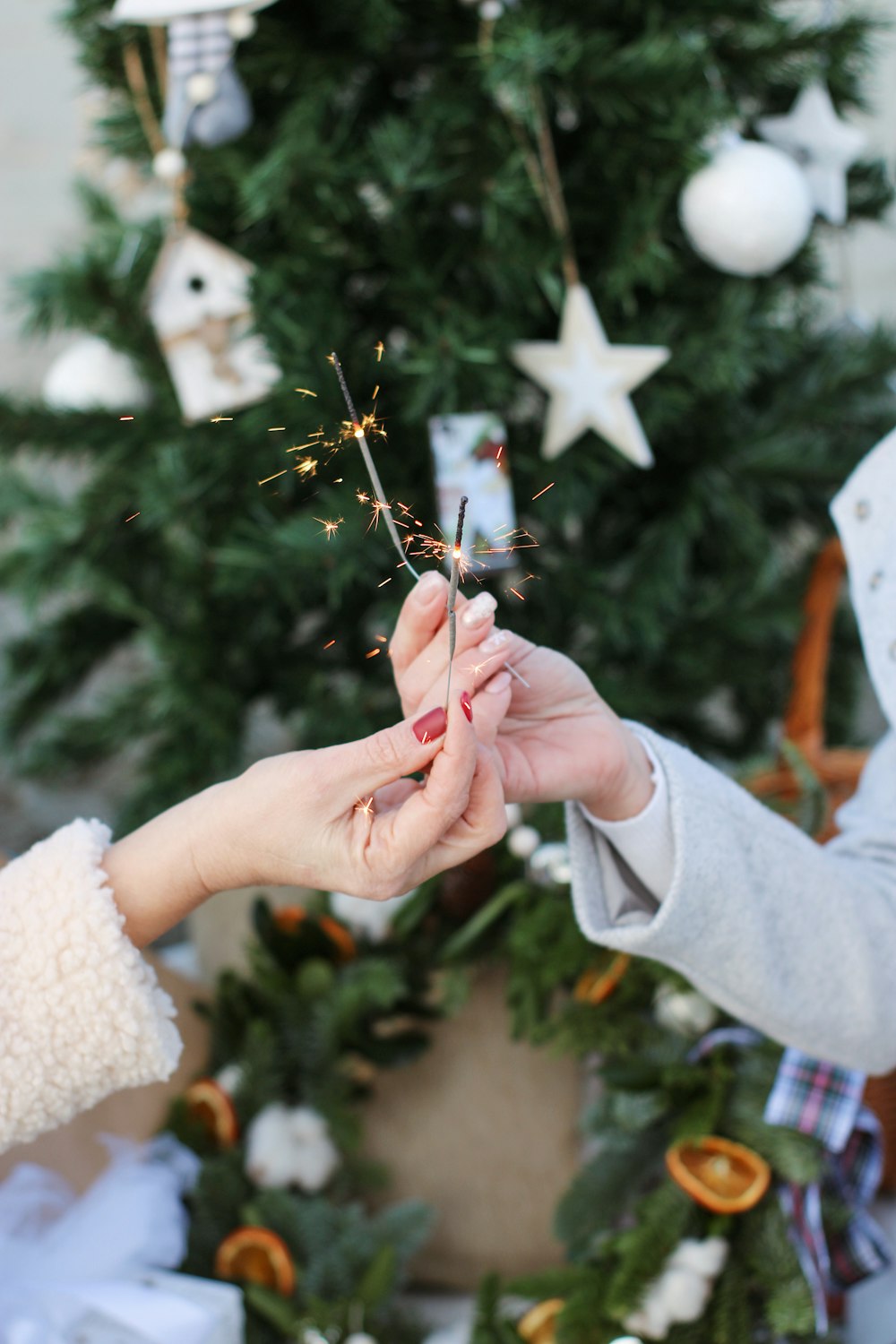 two people holding sparklers near a christmas tree