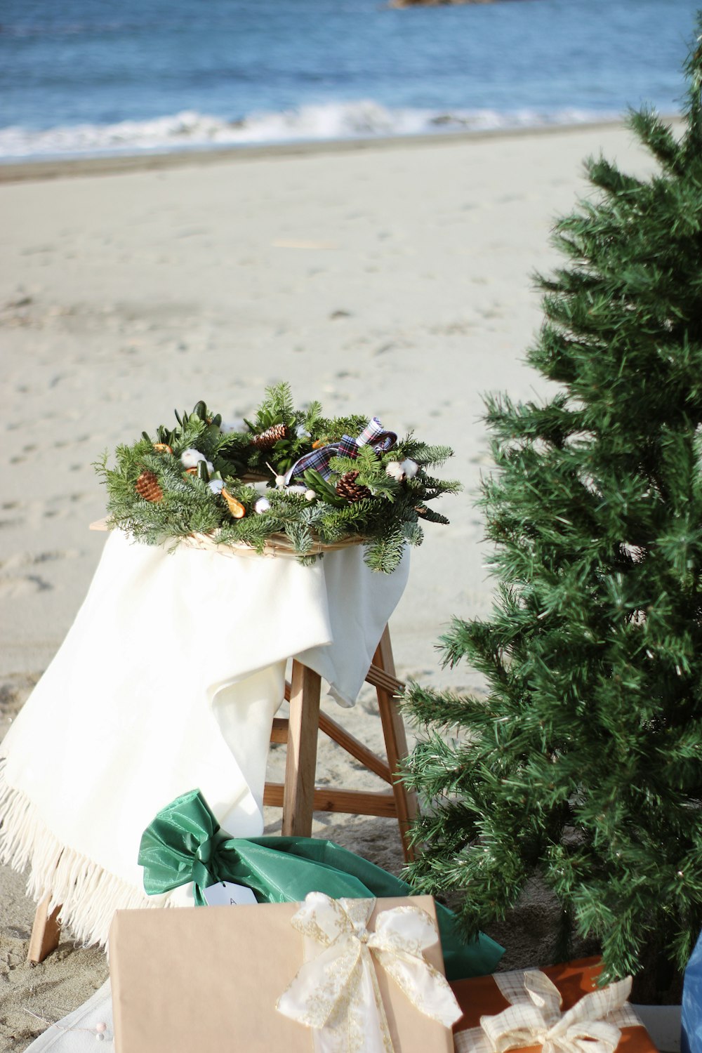 a christmas tree on the beach with presents under it