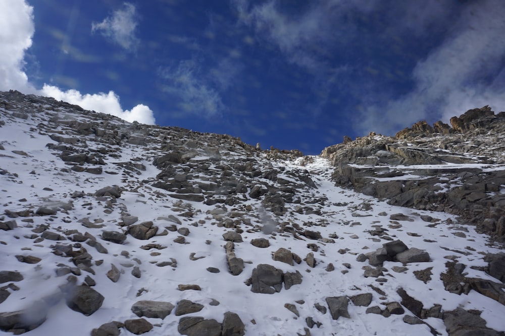a rocky mountain slope covered in snow under a cloudy blue sky