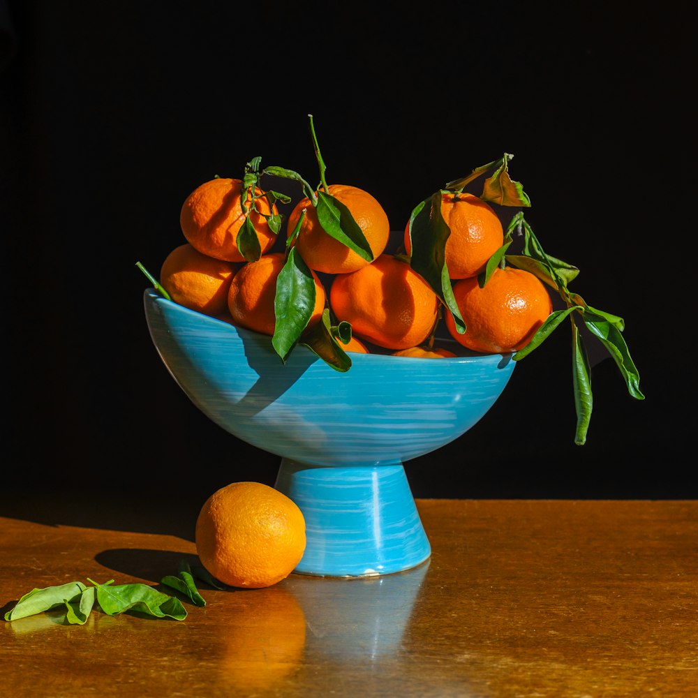 a blue bowl filled with oranges on top of a wooden table