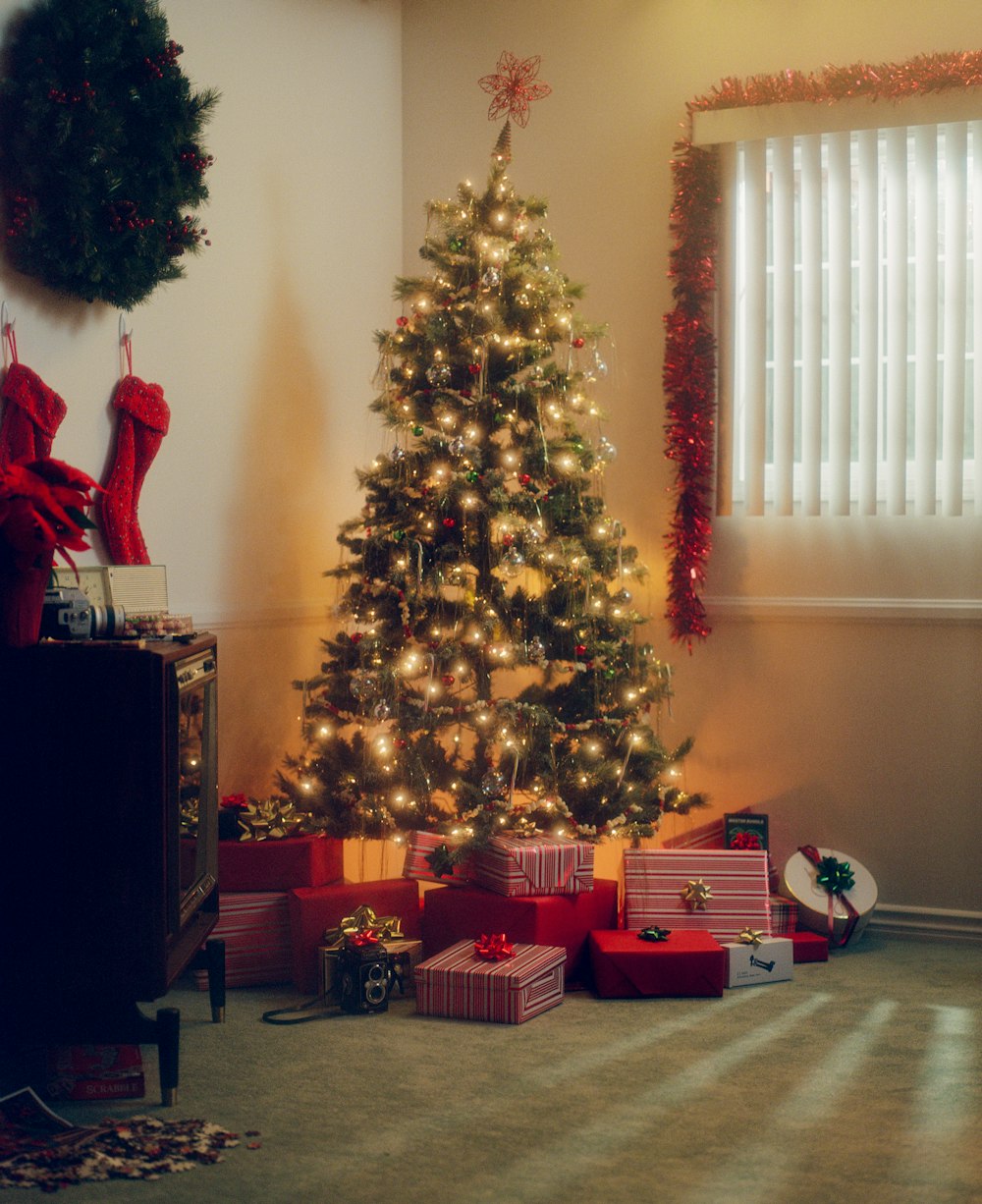 a christmas tree with presents under it in front of a window